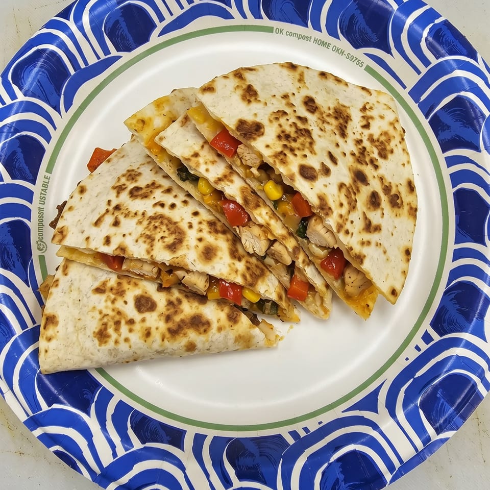 Chicken quesadillas with corn, red peppers, and black beans on a blue and white paper plate.