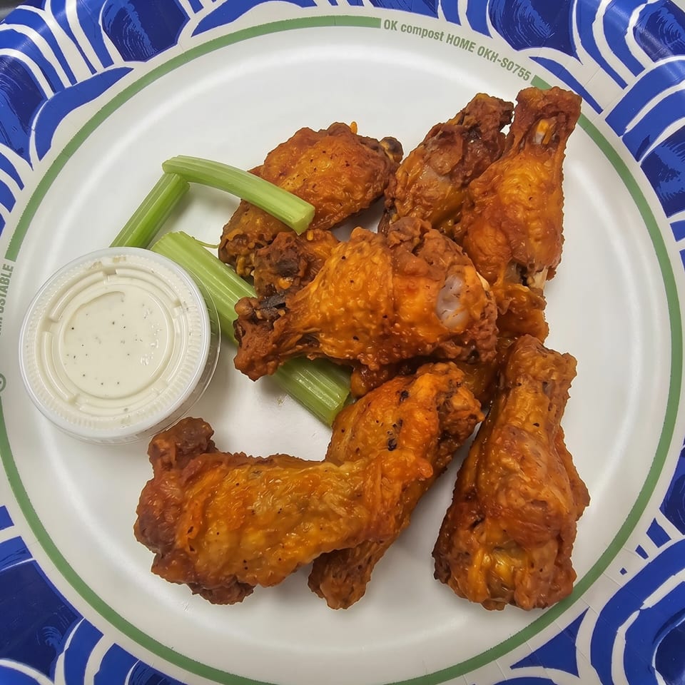 Buffalo wings with celery sticks and a side of ranch dressing on a paper plate.