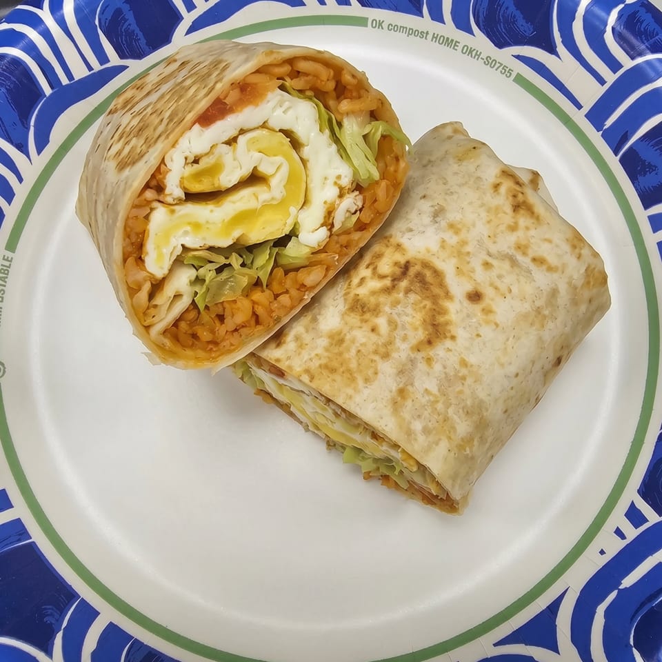 Two halves of a breakfast burrito with eggs, rice, and lettuce on a blue and white paper plate.
