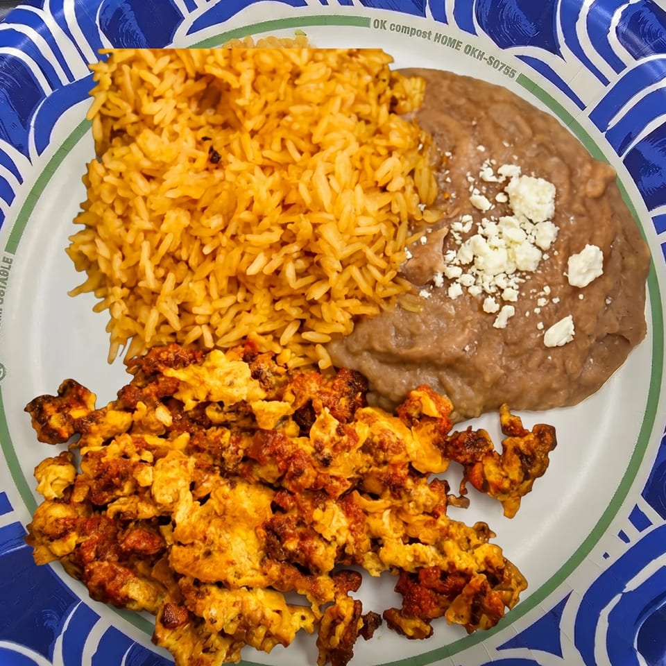 A paper plate with Mexican rice, refried beans topped with cheese, and scrambled eggs with chorizo.