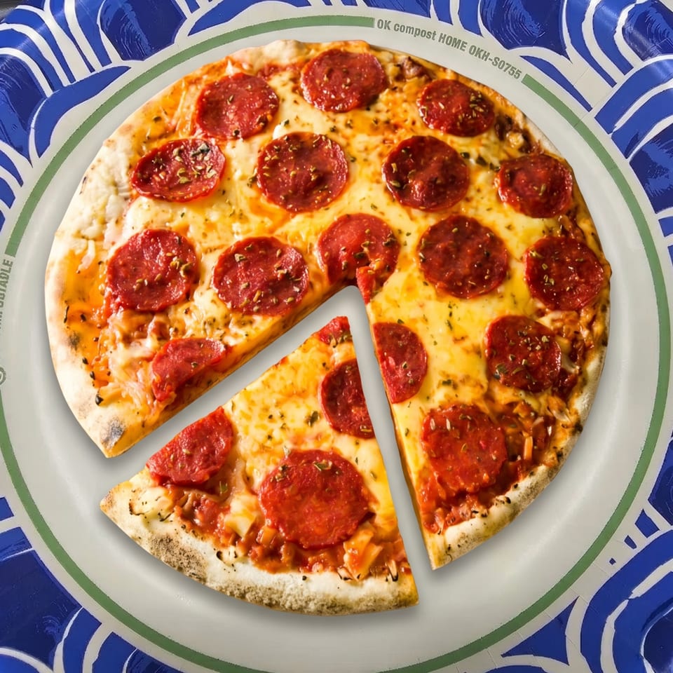 A pepperoni pizza with a slice removed, served on a blue and white patterned paper plate.