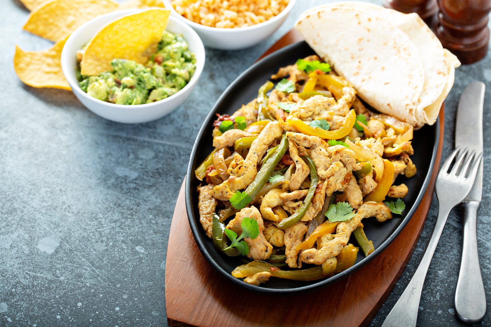 Chicken and bell peppers fajitas served in a cast iron pan with chips and guacamole